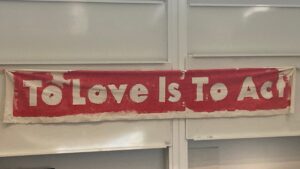 "To love is to act" written on a banner, white words on red background